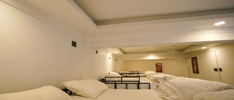 A hotel room with four single beds, a small table, and a ceiling fan.