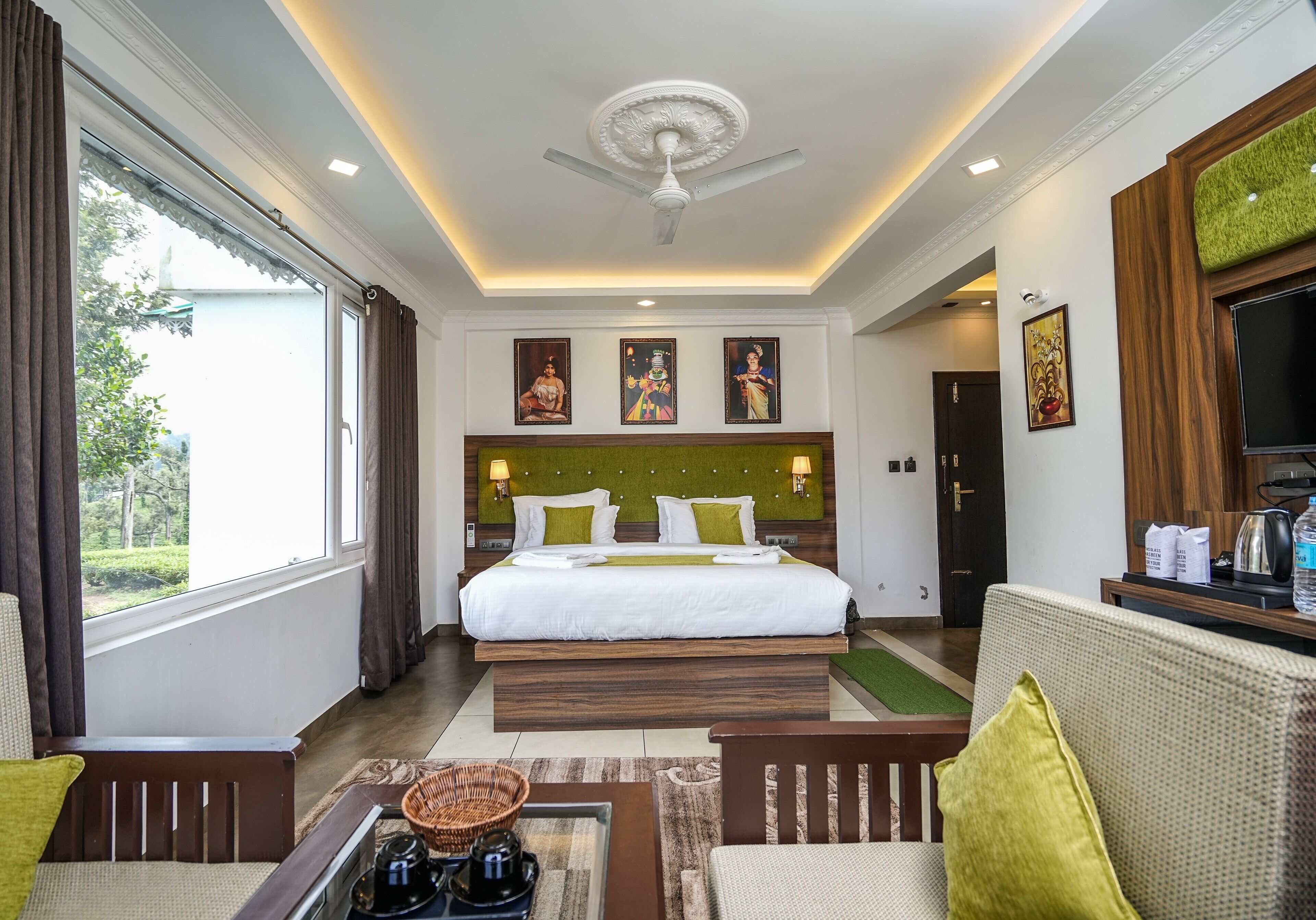 A hotel room with a large bed, a sofa, a coffee table, and a view of greenery outside.