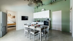 Een moderne keuken met witte kasten, een eettafel met stoelen, een koelkast, een aan de muur bevestigde televisie en een groene accentmuur.