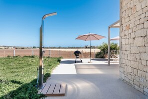 A patio area with a barbecue grill, an umbrella, and a stone wall.