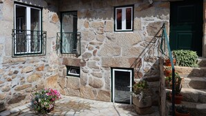 Un edificio de piedra con tejado de baldosas, varias ventanas, una escalera y plantas en macetas.