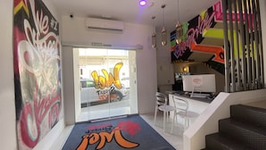 A modern interior with a reception desk, clear glass doors, and a colorful wall mural. - We Street Hostel - Albergue Juvenil (Palma de Mallorca)