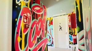 A hallway with colorful graffiti art on the walls, a white door at the end, and a fire extinguisher mounted on the wall. - We Street Hostel - Albergue Juvenil (Palma de Mallorca)