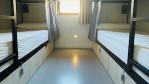 A narrow corridor with bunk beds on either side, a window at the end, and a light fixture on the wall. - We Street Hostel - Albergue Juvenil (Palma de Mallorca)