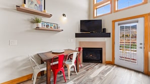 A dining area with a wooden table, red and white chairs, a fireplace, and a TV mounted above it. - Luxury Condo w/ 2 Private Balconies, Stunning Mountain Views & Natural Light! (Dillon)