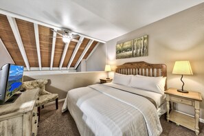 A bedroom with a large bed, a desk with a computer, a ceiling fan, and a window.