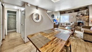 A spacious living area with a wooden dining table, a fireplace, and a stone accent wall. - Lakeland Village #310 Modern 1 bedroom+loft (South Lake Tahoe)