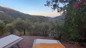 A patio with two sunbeds, a stone building, and a view of a valley with hills. - Detached Holiday Home on Olive Grove with Beautiful Sea View (Liguria)