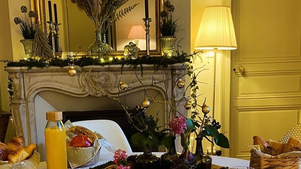 A dining table set with various dishes, a vase with flowers, and a fireplace in the background. - Chambre D'hôtes de Charme (Bernay)