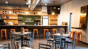 Un restaurante con varias mesas y sillas, una zona de bar con botellas y vasos, y un conducto de ventilación grande en el techo.