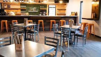 Un restaurante con varias mesas y sillas, una zona de bar con botellas y vasos, y un conducto de ventilación grande en el techo.