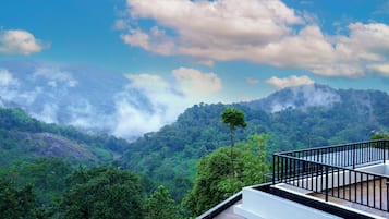 A view of a lush green valley with a mountain range in the background and a balcony with a railing.