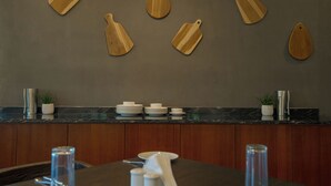 Une cuisine avec des planches à découper en bois accrochées au mur, un plan de travail en marbre et un coin repas avec une table dressée pour deux personnes.