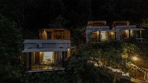 Un immeuble moderne à plusieurs étages, doté de grandes fenêtres et de balcons, et entouré d’une végétation luxuriante.