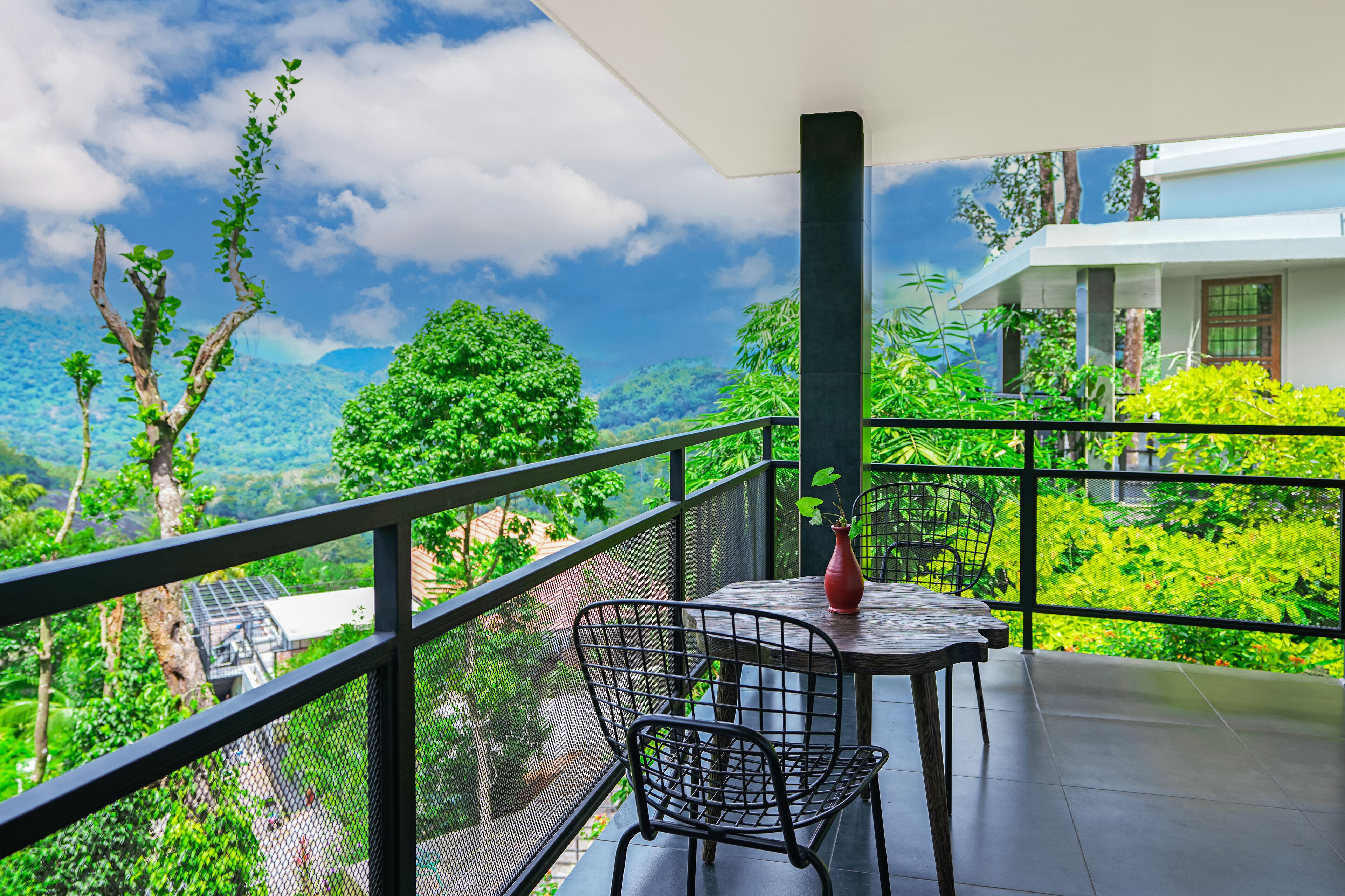 Un balcon avec une table et des chaises, offrant une vue sur une végétation luxuriante et un paysage montagneux.