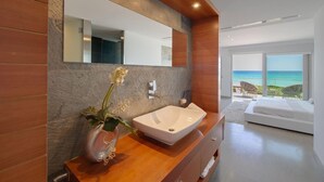 Un baño moderno con un espejo grande, un lavabo blanco y un florero con flores.