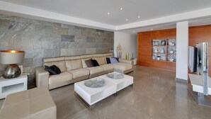 Una sala moderna con un sofá beige, dos mesas de centro blancas y una pared de piedra.
