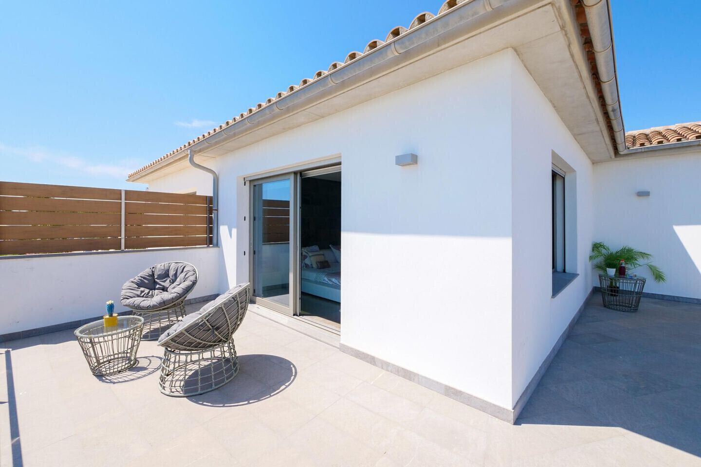 Une terrasse moderne avec une porte-fenêtre coulissante donnant sur une chambre, une chaise, une petite table et une plante en pot.