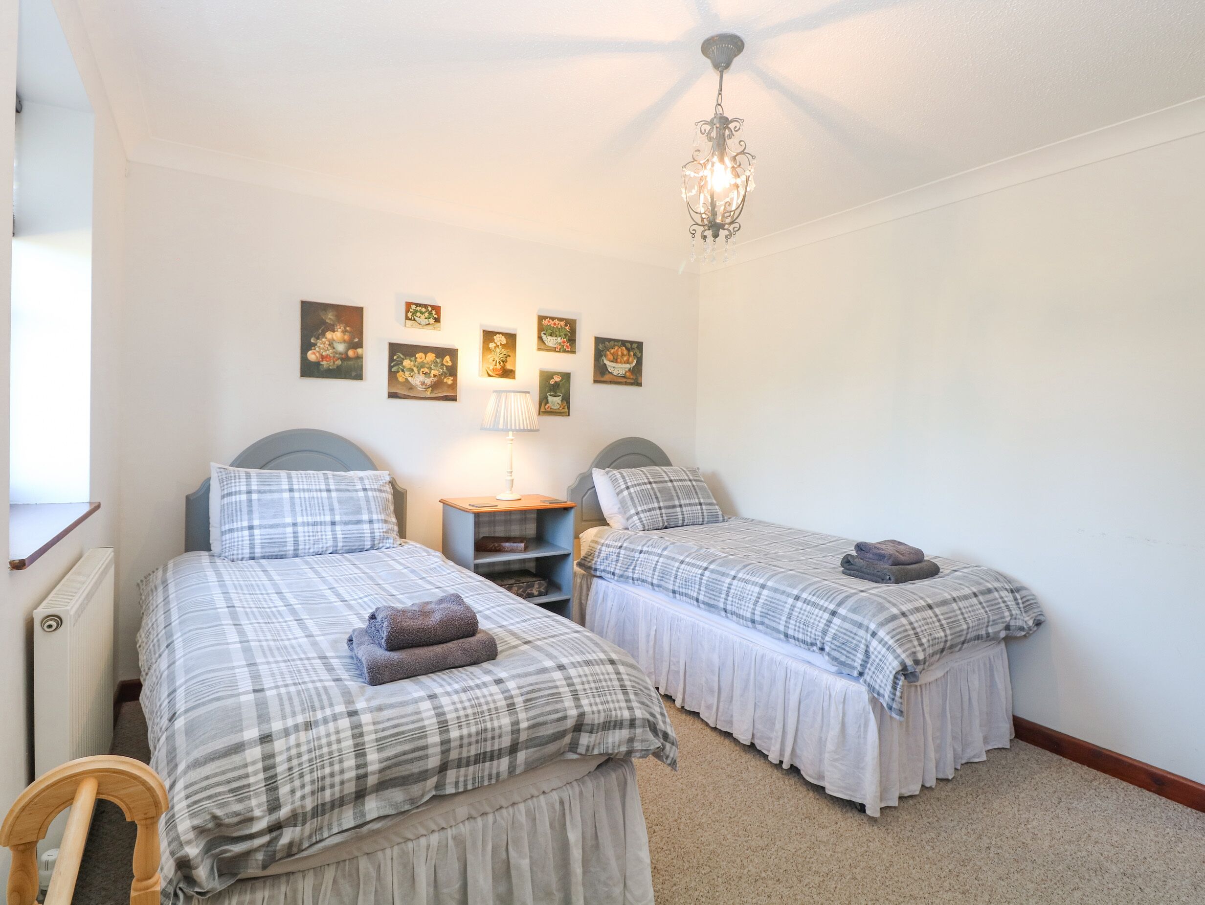 A bedroom with two beds, a chandelier, and wall art.