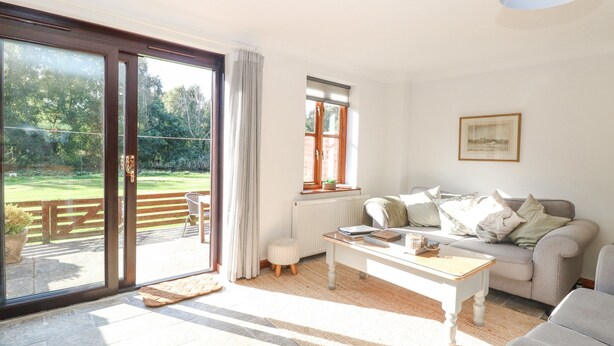 Un salón luminoso con un sofá, una mesa de centro y vistas a un jardín a través de una puerta corrediza de vidrio.