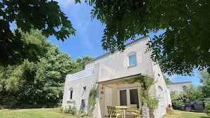 A two-story stone building with a small patio area, a table and chairs, and a car parked nearby. - Prachtig Designhuis, Rustige Ligging, Zwembad, Speeltuin, Fietsen in de Duinen (De Cocksdorp)