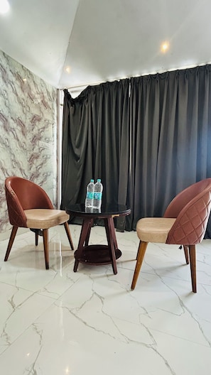 A room with a marble floor, two leather chairs, a small table with water bottles, and a black curtain backdrop. - Raha Resort (Udaipur)