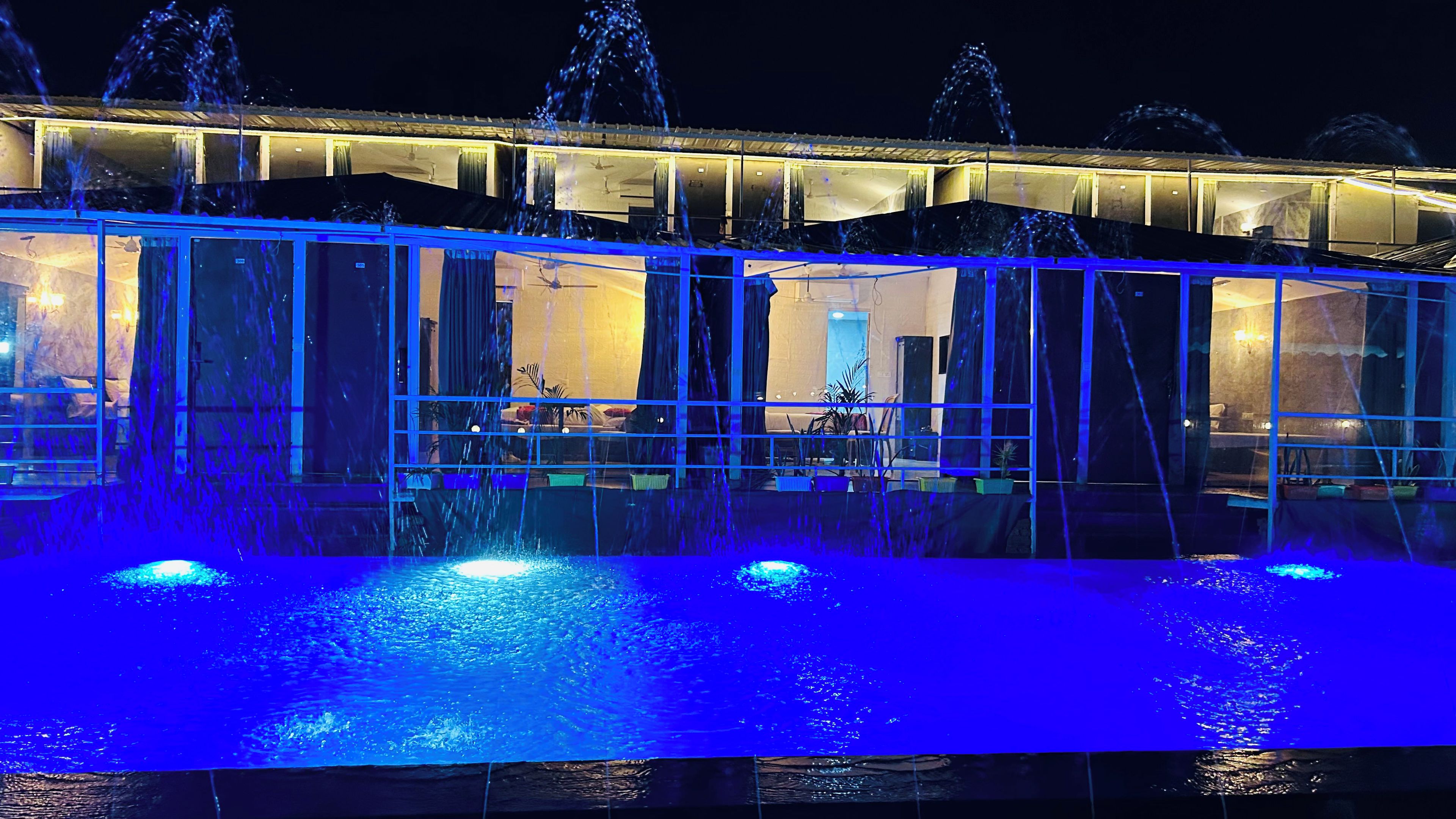 Un edificio con una fuente en primer plano, una zona de estar al aire libre techada y un interior bien iluminado.