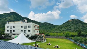 A building with multiple windows and a flat roof, surrounded by lush greenery and hills. - Raha Resort (Udaipur)