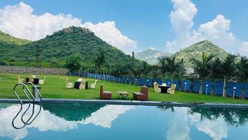 A poolside area with lounge chairs and a table, surrounded by a stone wall and a view of green hills.