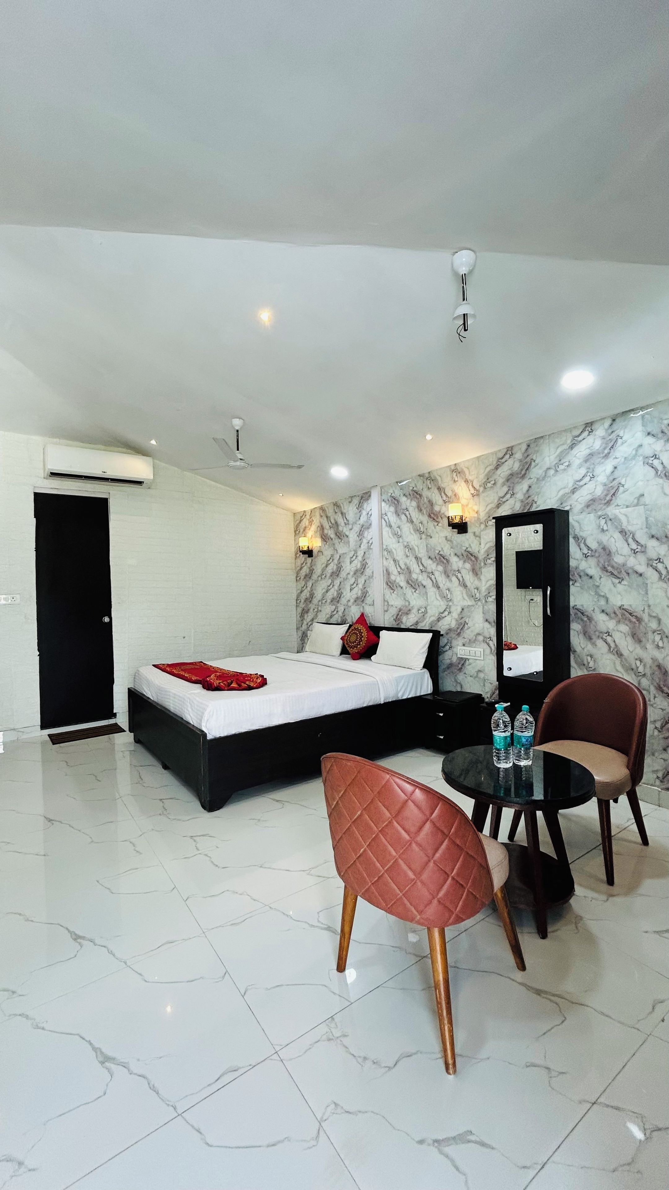 Habitación de hotel con cama, escritorio, dos sillas, espejo y pared con diseño de mármol.