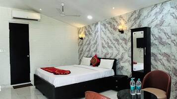 Habitación de hotel con cama, escritorio, dos sillas, espejo y pared con diseño de mármol.