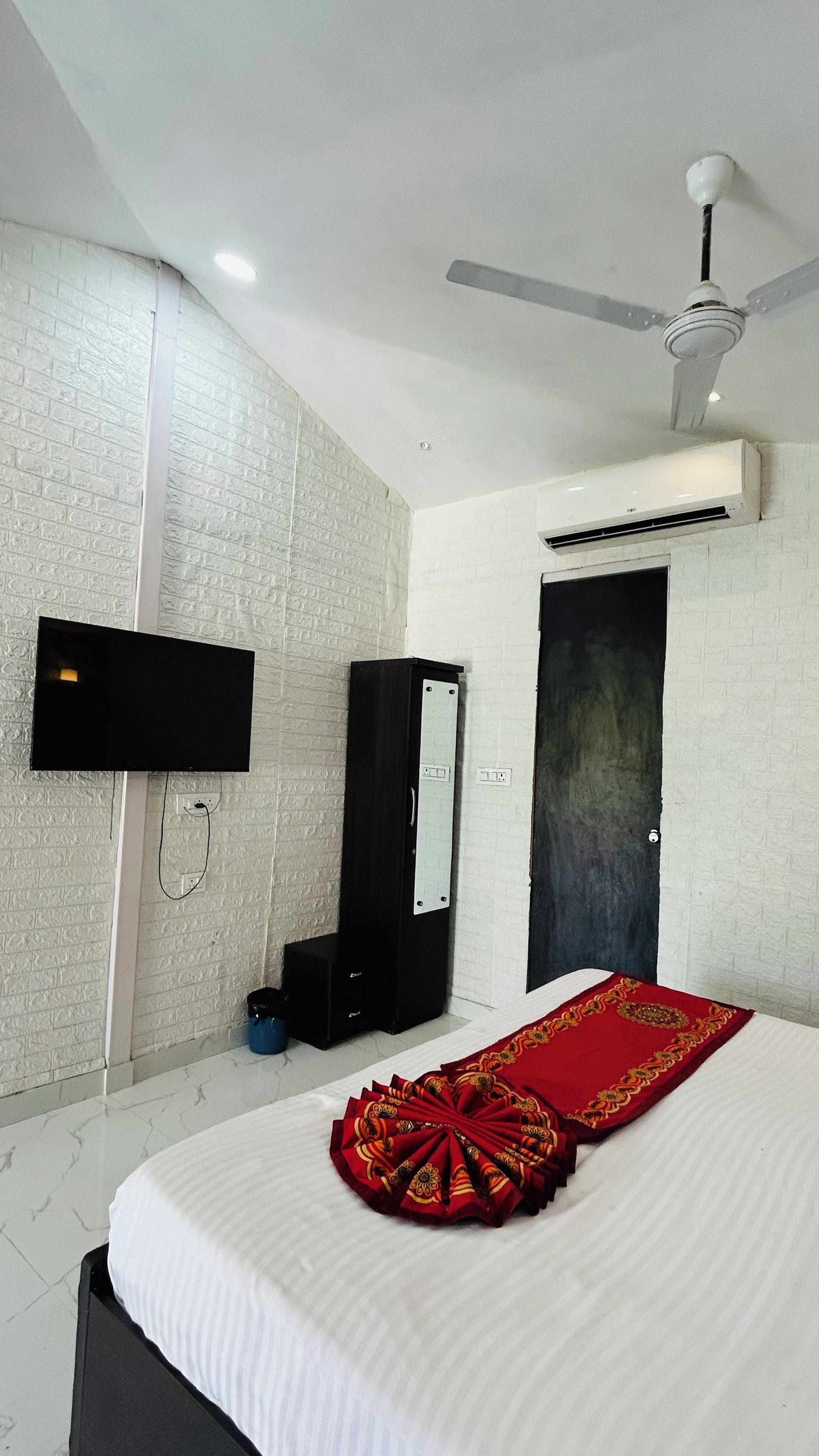 Habitación de hotel con cama, televisor de pantalla plana montado en la pared, ventilador de techo y aire acondicionado.