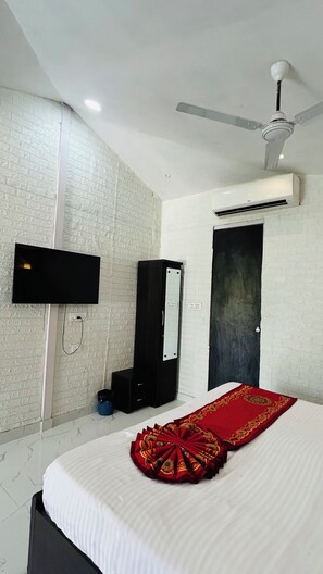 A hotel room with a bed, a flat-screen TV mounted on the wall, a ceiling fan, and an air conditioning unit. - Raha Resort (Udaipur)