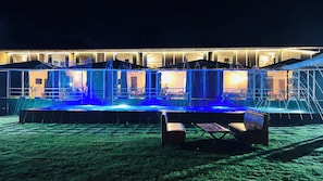A hotel with a pool area, outdoor seating, and a well-lit facade at night.