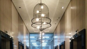 Un corridoio moderno con ascensori, un pavimento lucido e un lampadario centrale.