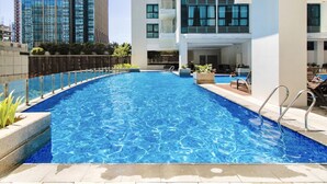 Una piscina con superficie d'acqua cristallina e azzurra, circondata da un bordo piastrellato e una ringhiera di sicurezza metallica.