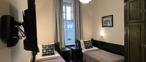 Een hotelkamer met twee bedden, een bureau met stoel, een aan de muur bevestigde televisie, een raam met gordijnen en een kast.