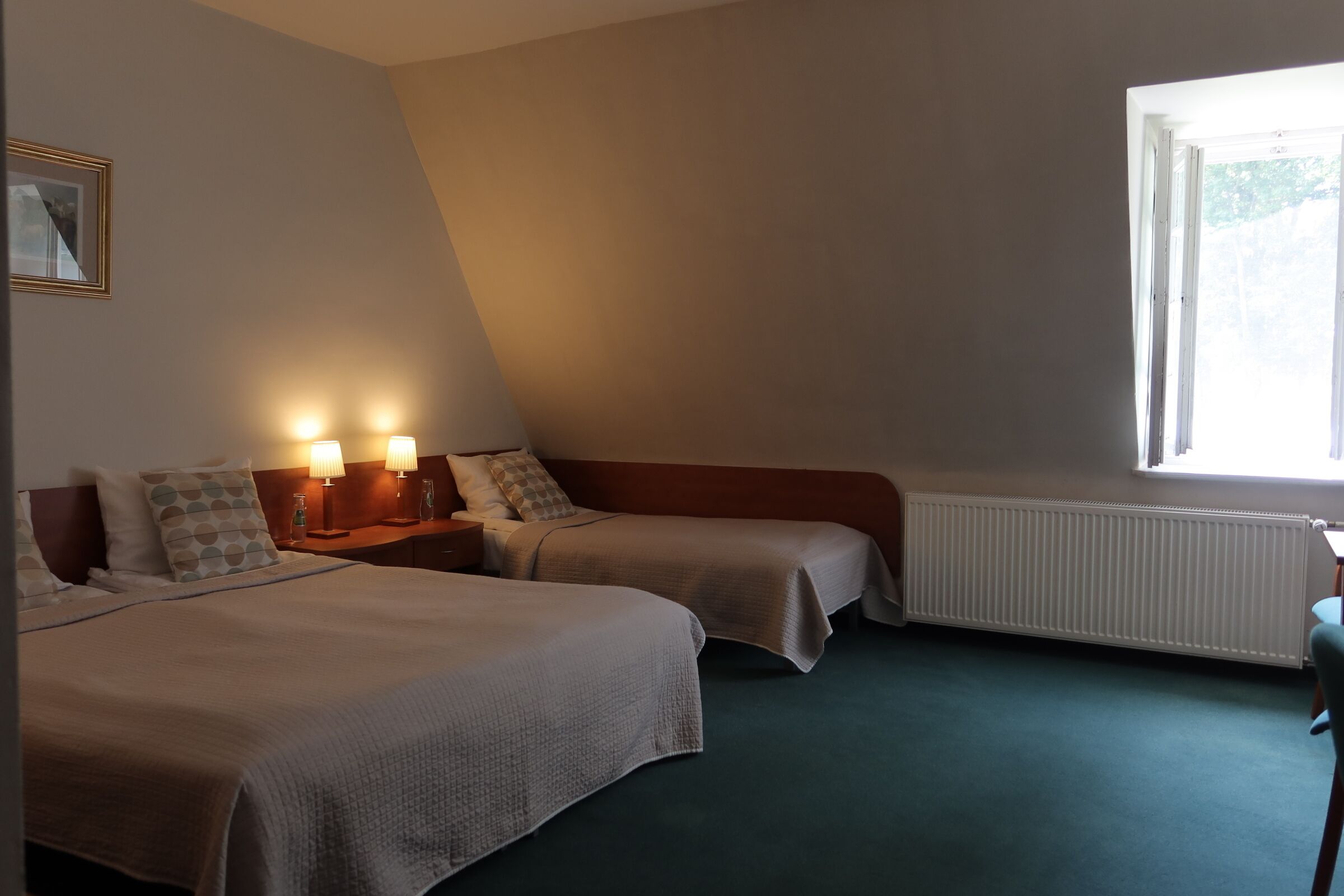 A hotel room with two beds, a window, a radiator, and bedside lamps.