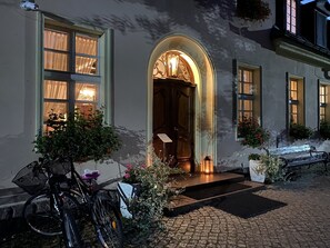 Un bâtiment à la façade en pierre, une porte en bois surmontée d’un arc, et un vélo garé à l’extérieur.