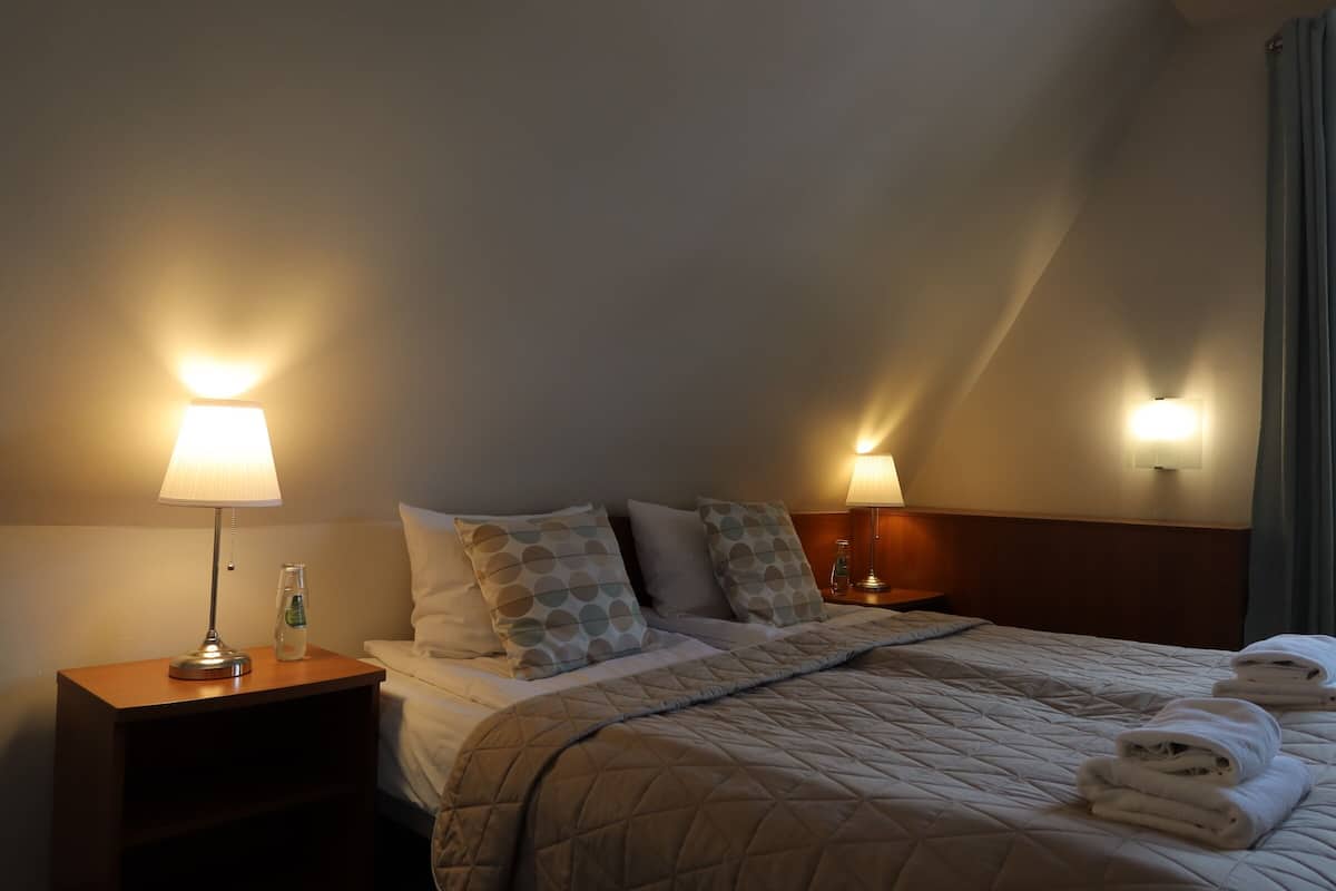 Una habitación de hotel con una cama, dos lámparas de noche, una mesita de noche y una ventana con cortinas.