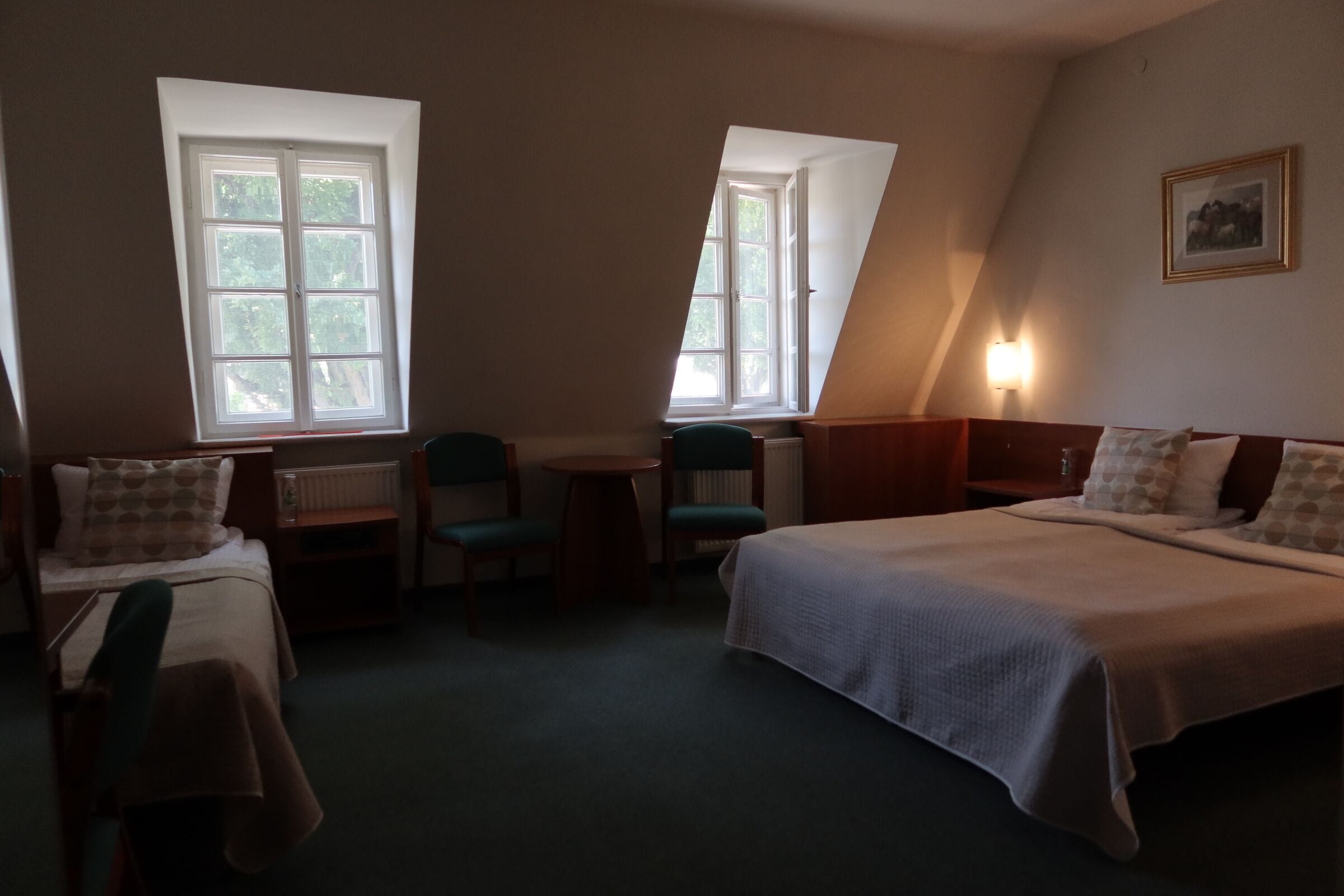 Una habitación con dos camas, una mesita, dos sillas y dos ventanas.