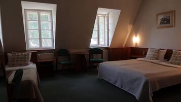 Una habitación con dos camas, una mesita, dos sillas y dos ventanas.