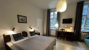 Un dormitorio con una cama grande, un escritorio, una silla, un televisor y una ventana con cortinas.