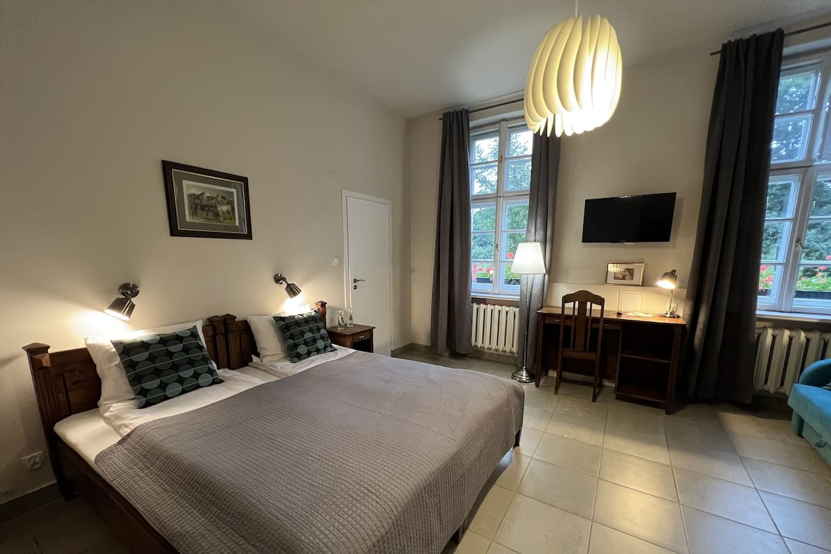Un dormitorio con una cama grande, un escritorio, una silla, un televisor y una ventana con cortinas.