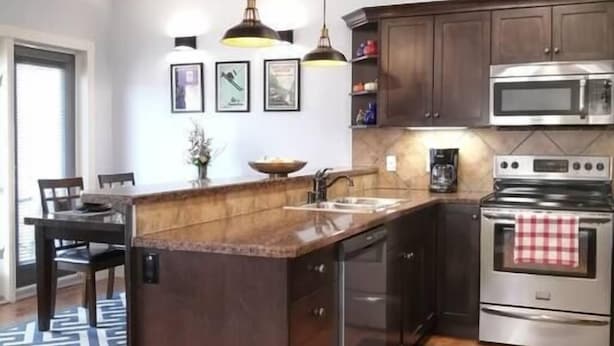 Una cocina moderna con armarios oscuros, electrodomésticos de acero inoxidable, iluminación colgante y una isla central.