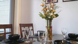 Una mesa de comedor dispuesta con cuencos negros, copas de vino y un florero con flores.