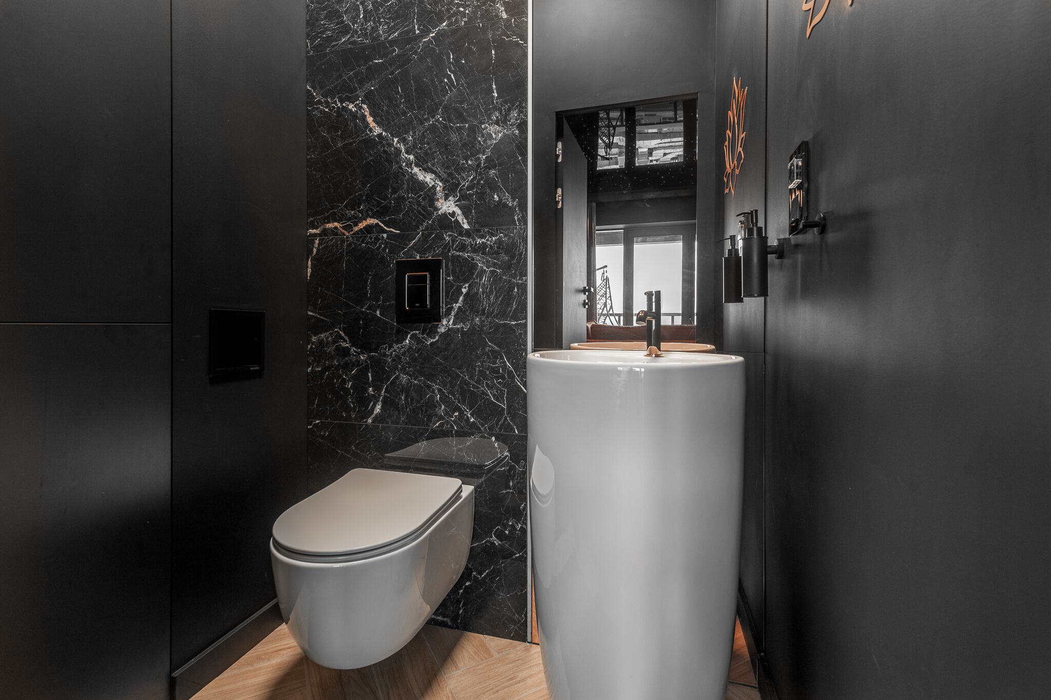 A modern bathroom with a marble wall, a white toilet, and a large sink.