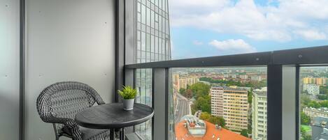 A balcony with a wicker chair and a small table, a potted plant, and a city view.