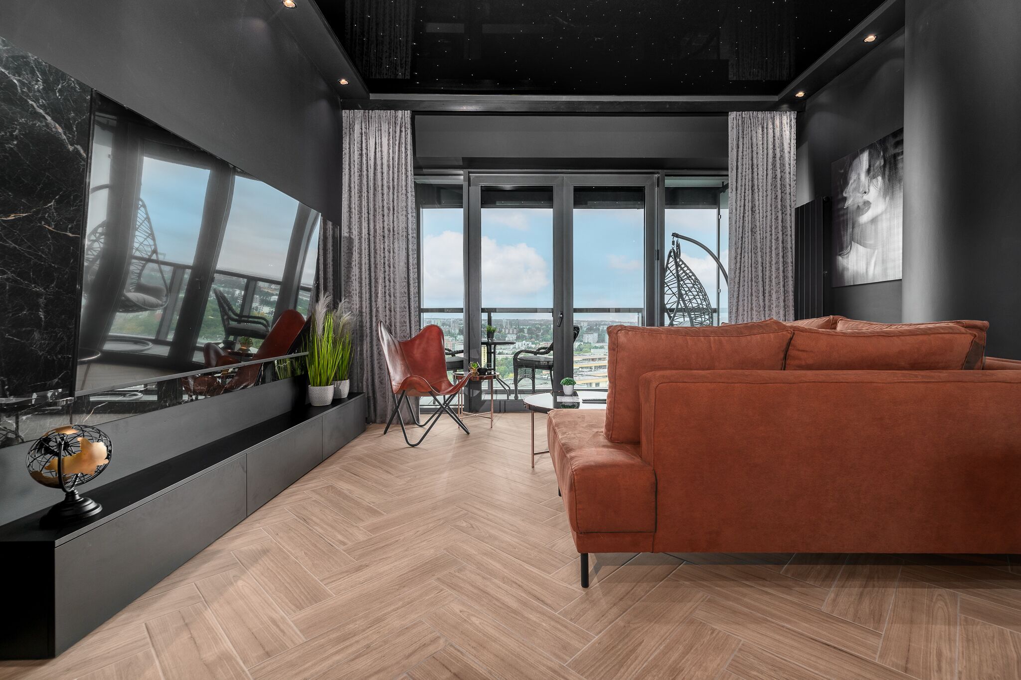 Una sala moderna con un televisor de pantalla plana grande, un sofá, una zona de comedor con sillas y vistas a la ciudad a través de amplios ventanales.