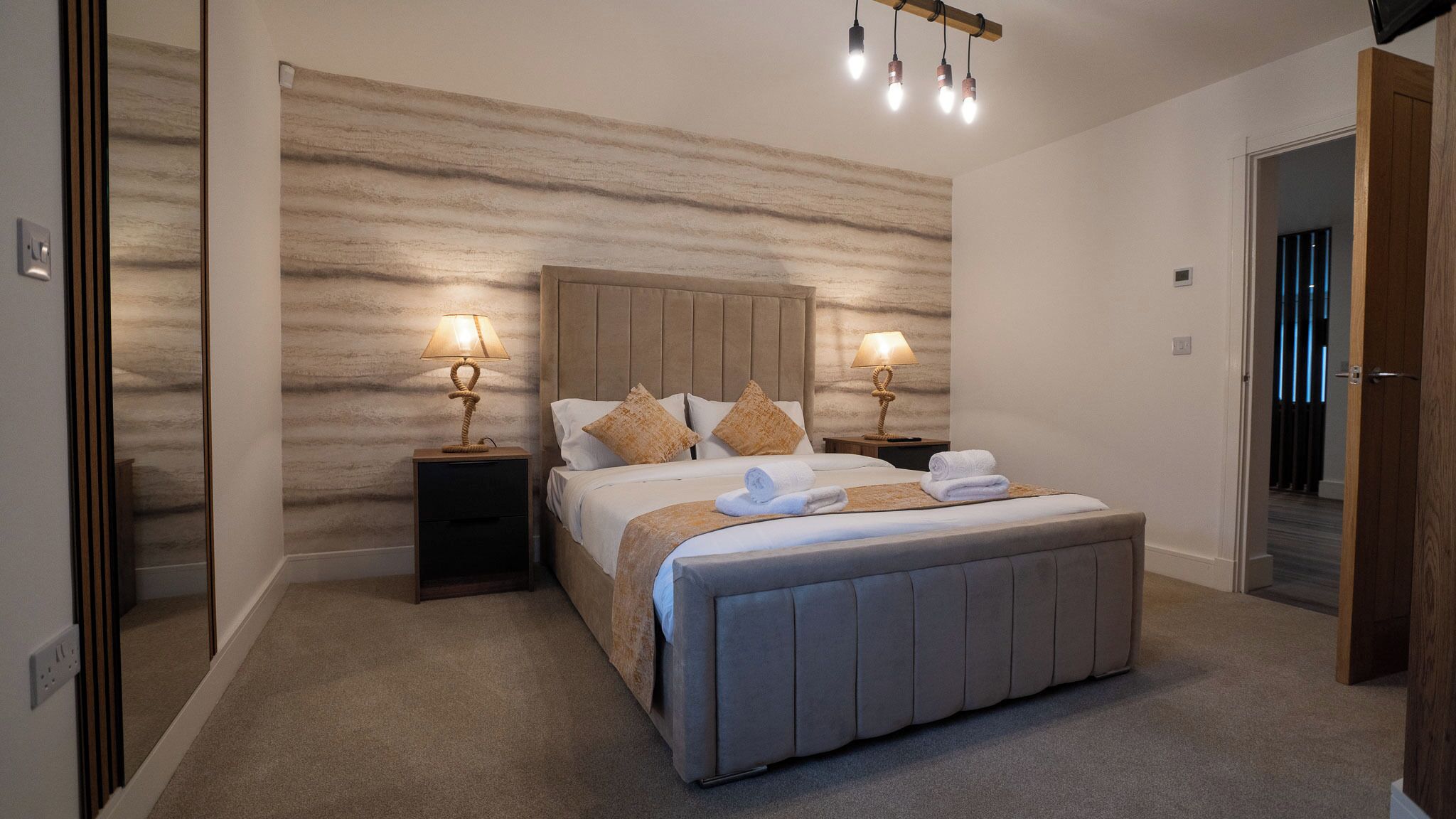 A modern bedroom with a large bed, two bedside tables with lamps, a wooden headboard, and a textured wall.